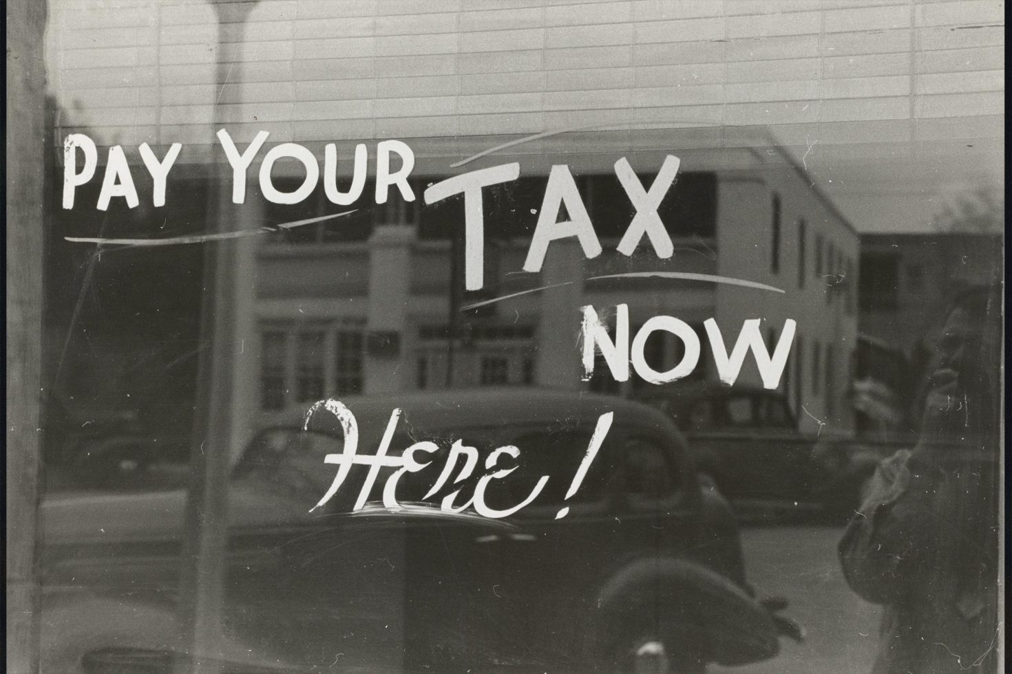 Vintage Image of a shop window with 'Pay your tax now Here!' painted on it.