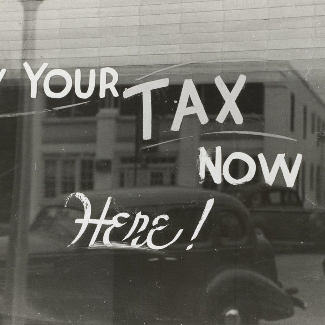 Vintage Image of a shop window with 'Pay your tax now Here!' painted on it.